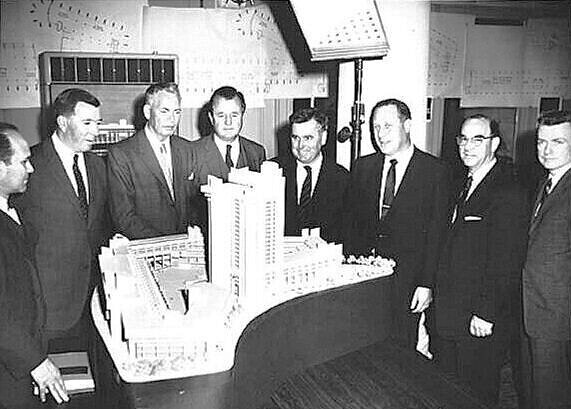 Key players at the creation of the Boston Government Service Center. In the foreground is a model of the complex, with the Hurley Building closest to the front of the picture (the model also includes the unbuilt office tower.) In the background are architectural drawings of the complex: an elevation and numerous floor plans. Among the people assembled for the photo are Edward Logue and Paul Rudolph (who is standing at far right.)